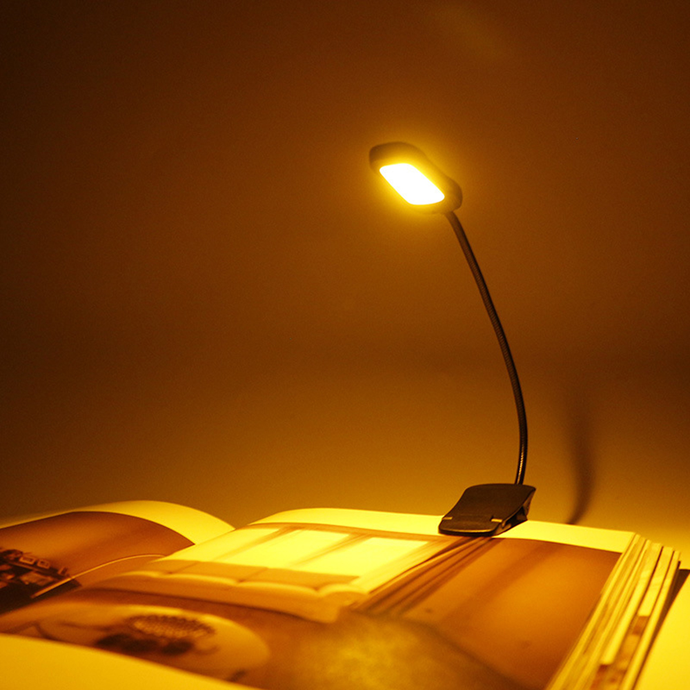 Eine kleine Leselampe ist an ein offenes Buch geklemmt. Das Licht scheint auf die Seiten. Der Hintergrund ist ein Gelb-Braun-Verlauf.