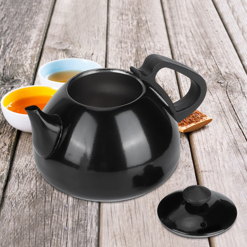 Eine schwarze Teekanne mit Deckel steht auf einem Holztisch. Zwei kleine Schalen mit Tee stehen hinter der Teekanne. Ein Holzlöffel mit Teeblättern.