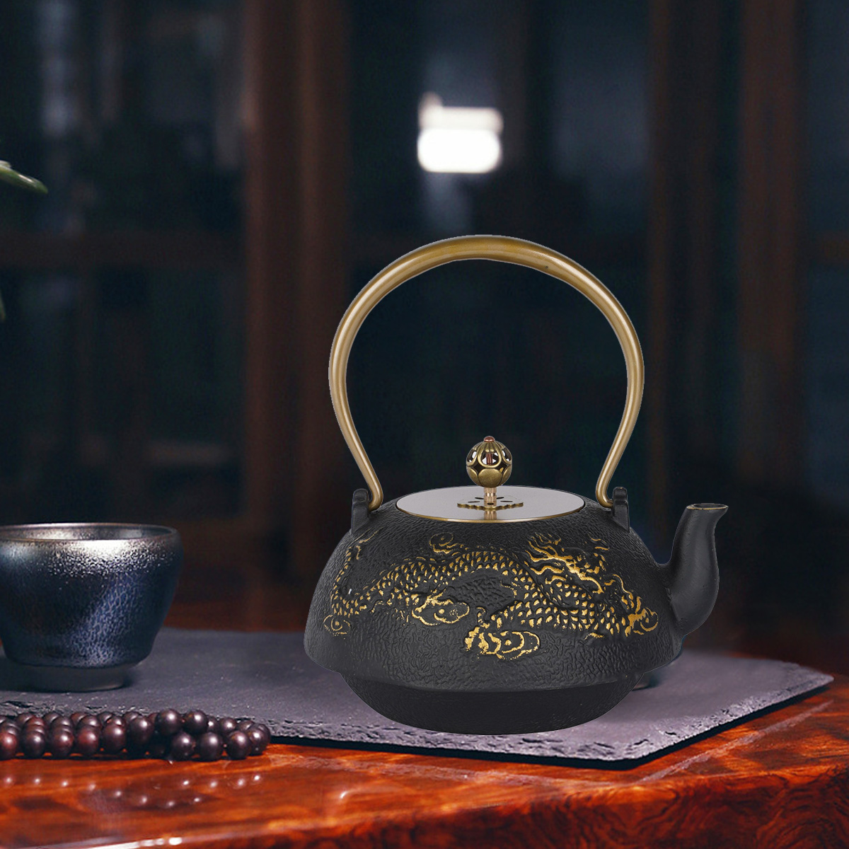 Schwarze Teekanne mit goldenem Drachendesign, goldenem Griff, auf Schiefer mit Tasse und Perlen. Dunkler Hintergrund.