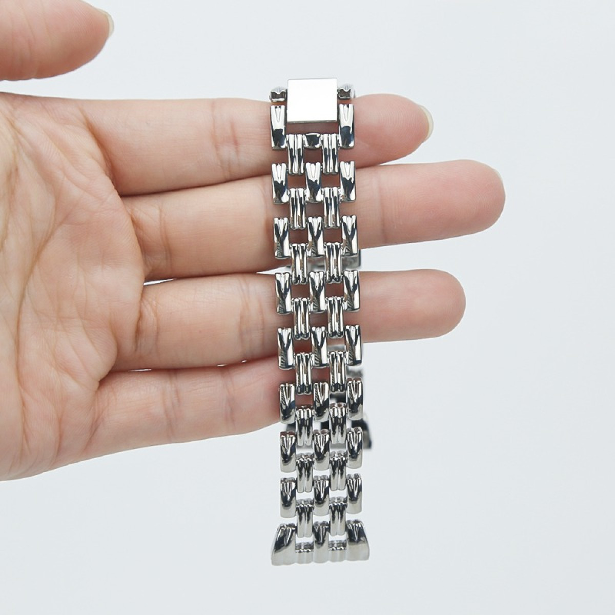 Eine Hand hält ein silbernes Uhrenarmband vor weißem Hintergrund. Das Armband besteht aus verbundenen, rechteckigen Metallstücken.