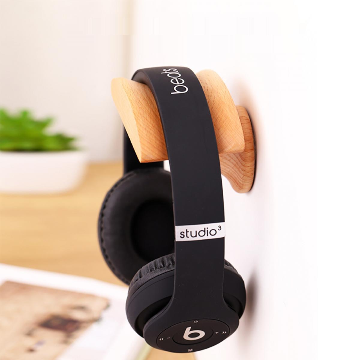 Schwarze Beats-Kopfhörer hängen an einer hölzernen Wandhalterung. Weiße Wand im Hintergrund, mit Pflanze und Buch sichtbar.
