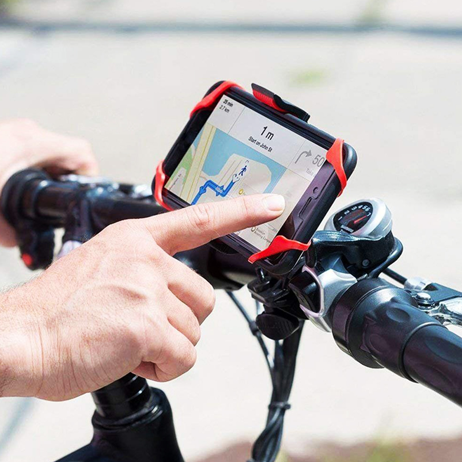 Un telefono con mappa è montato sul manubrio di una bici. Un dito tocca lo schermo. Cinghie rosse fissano il telefono.