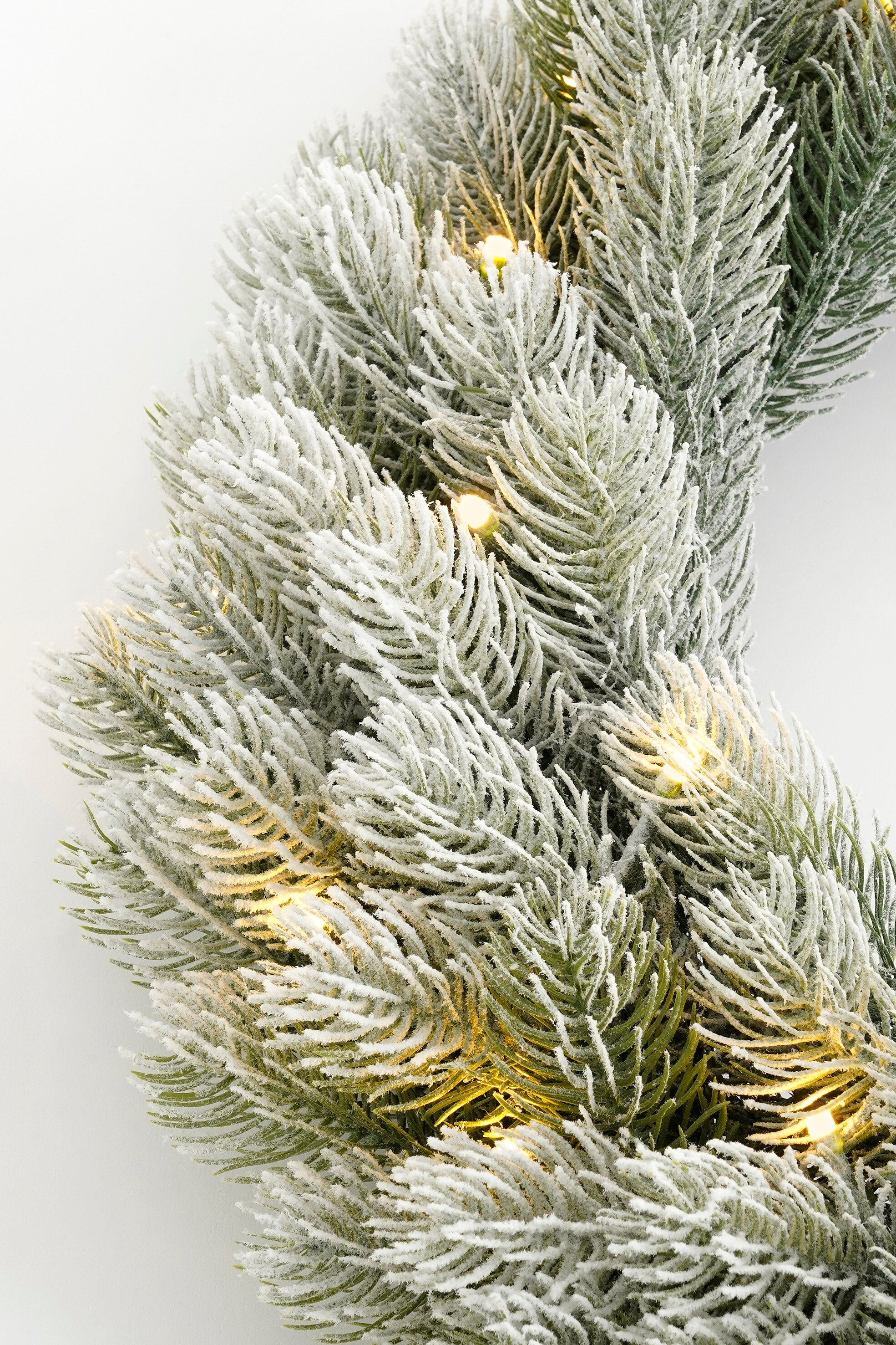Gros plan d'une couronne de Noël givrée avec des lumières scintillantes.