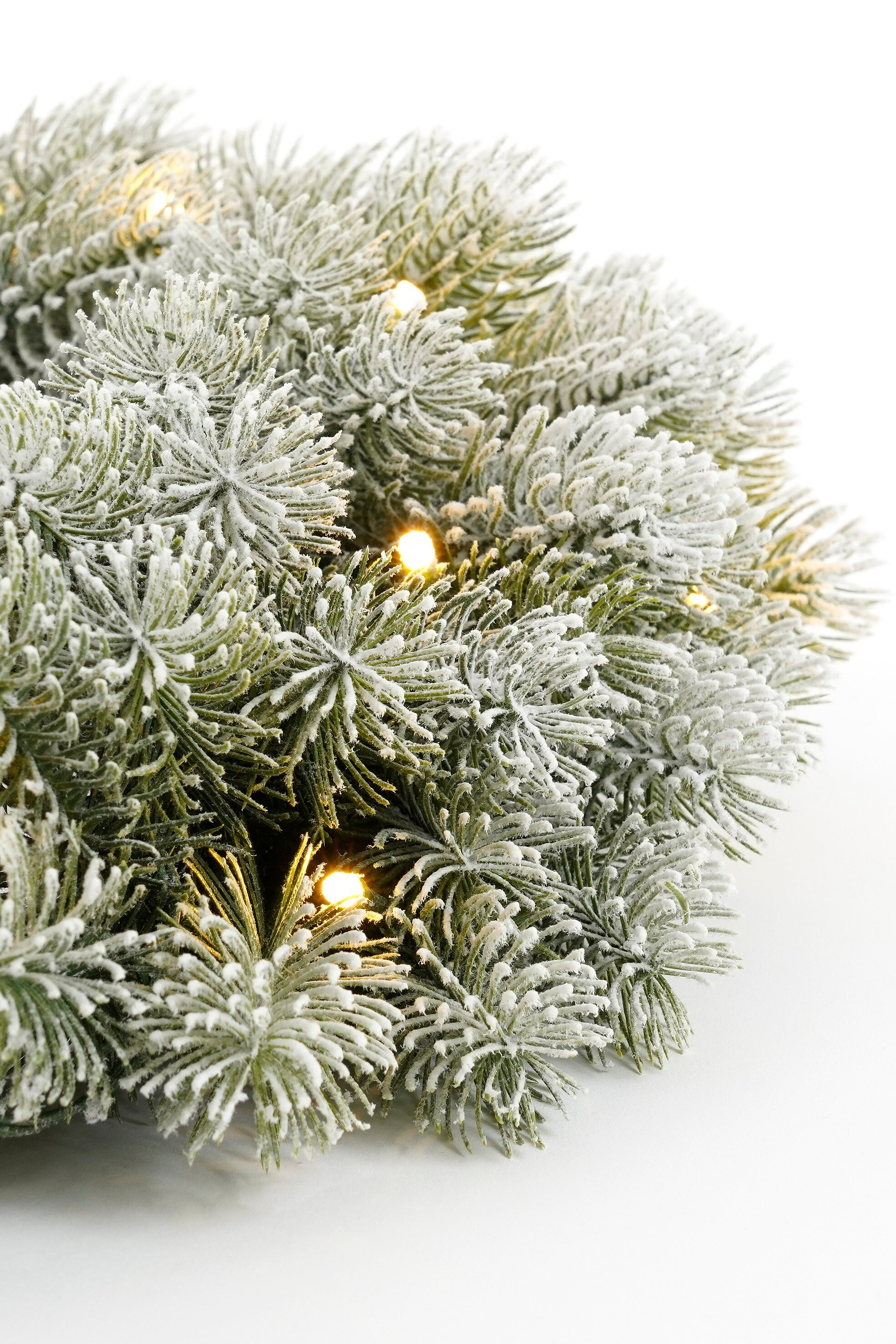 Gros plan d'une couronne de Noël givrée avec de petites lumières sur fond blanc. Aiguilles vertes et givre blanc.