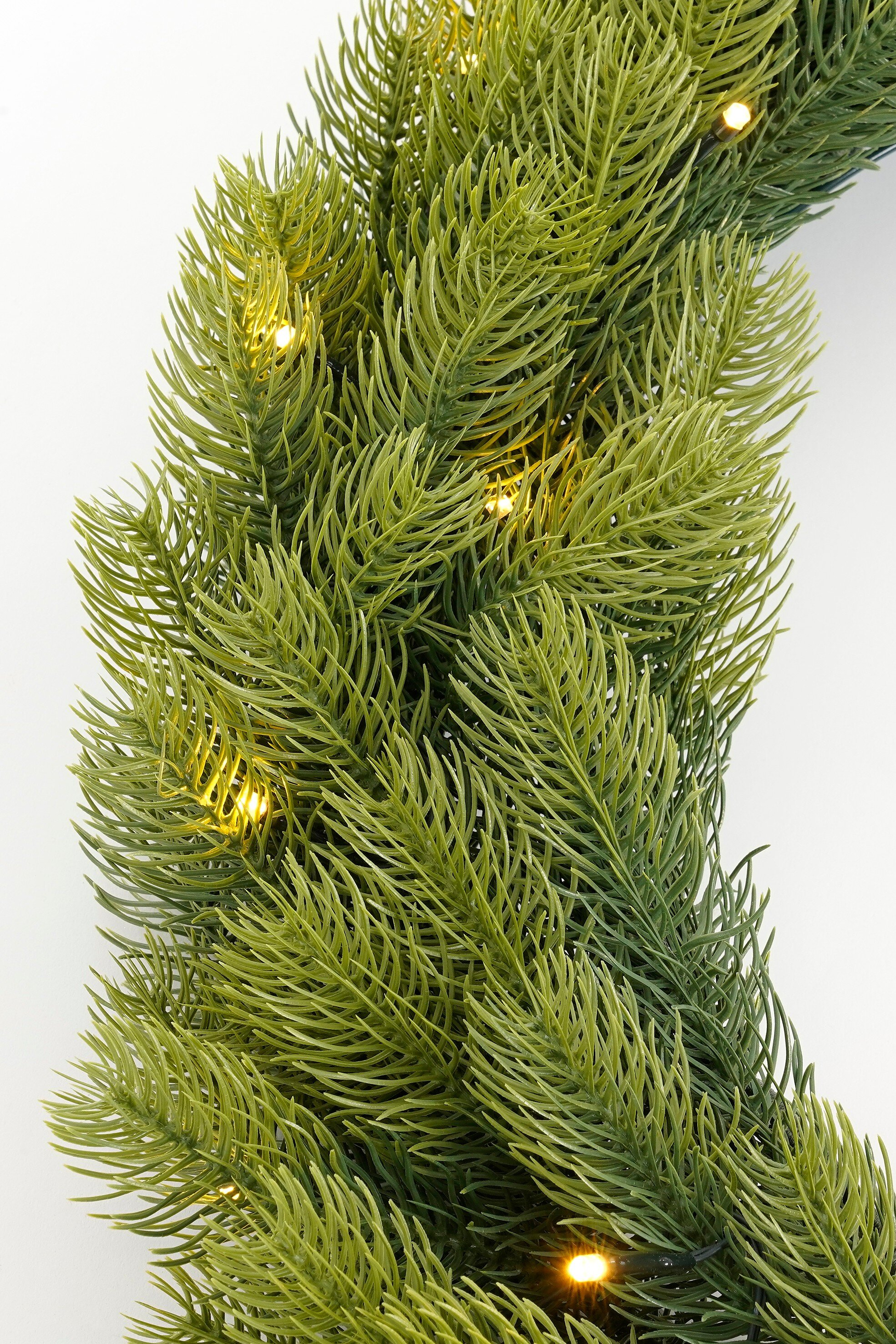 Gros plan d'une couronne de Noël verte avec de petites lumières, sur fond blanc.