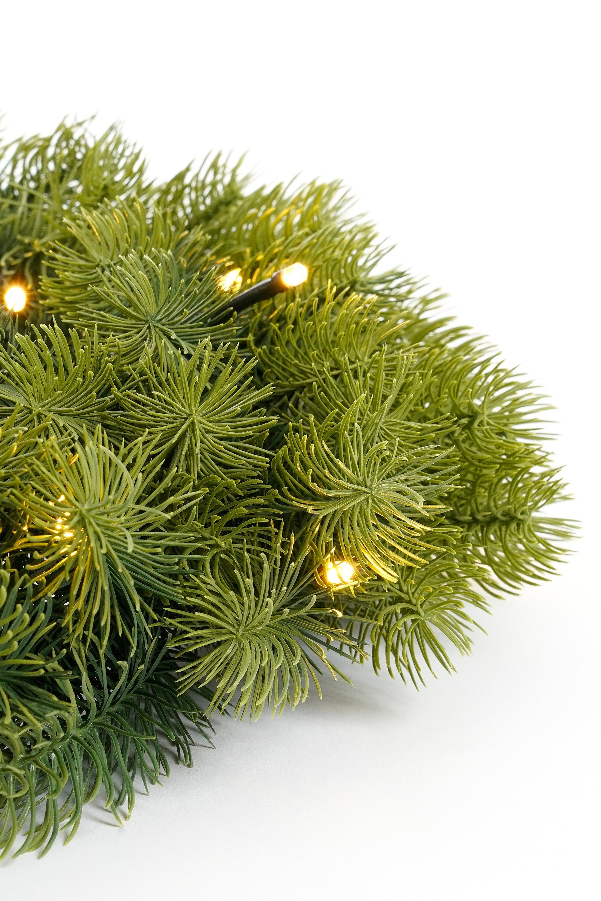 Gros plan d'une guirlande de sapin verte avec des lumières blanches chaudes sur fond blanc.