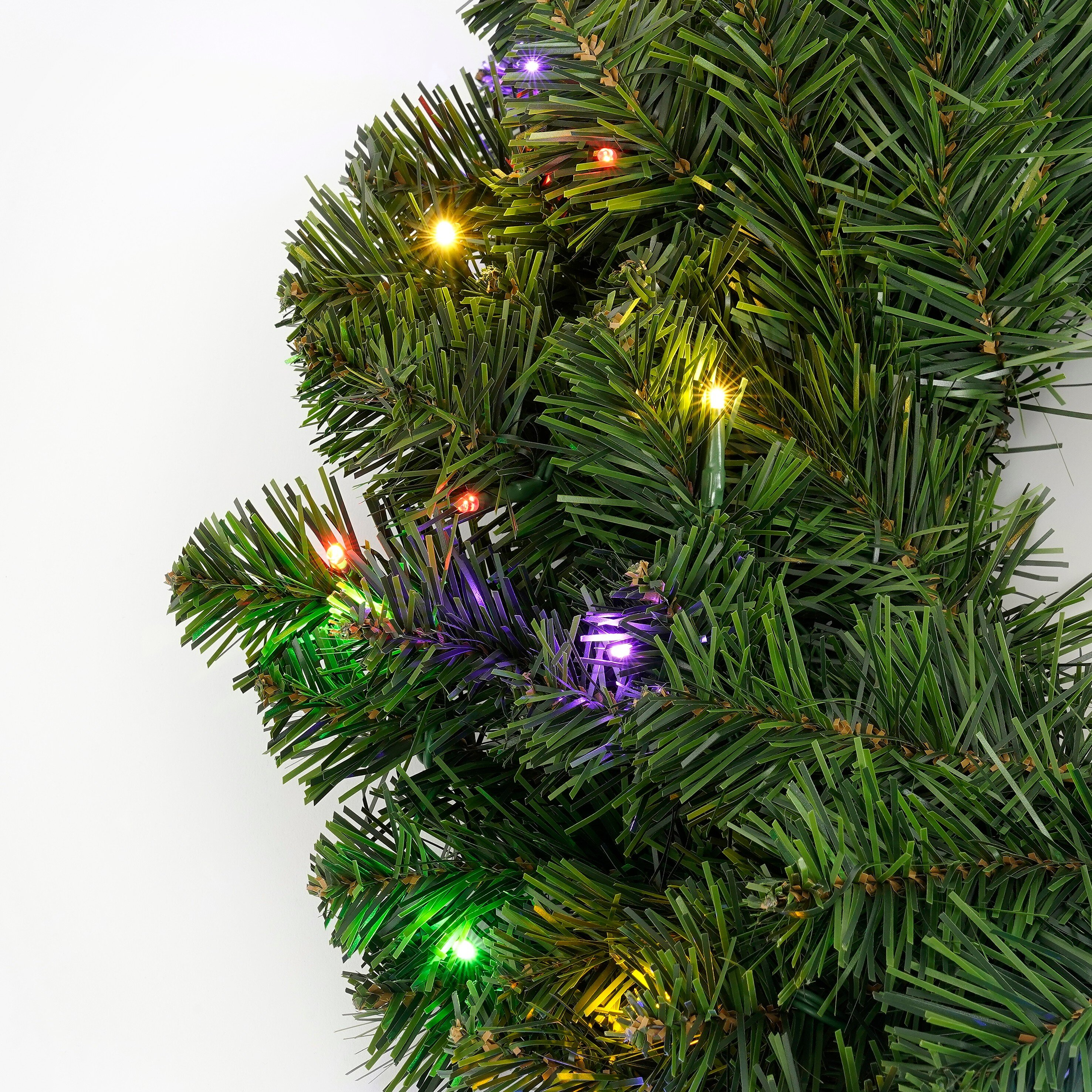 Gros plan d'une guirlande de Noël verte avec des lumières colorées sur fond blanc.
