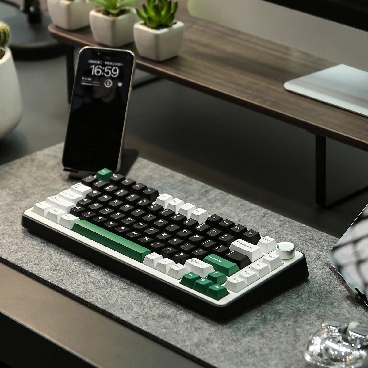 Un clavier moderne avec des touches noires, blanches et vertes est posé sur un bureau. Un téléphone affiche l'heure. Petites plantes en arrière-plan.