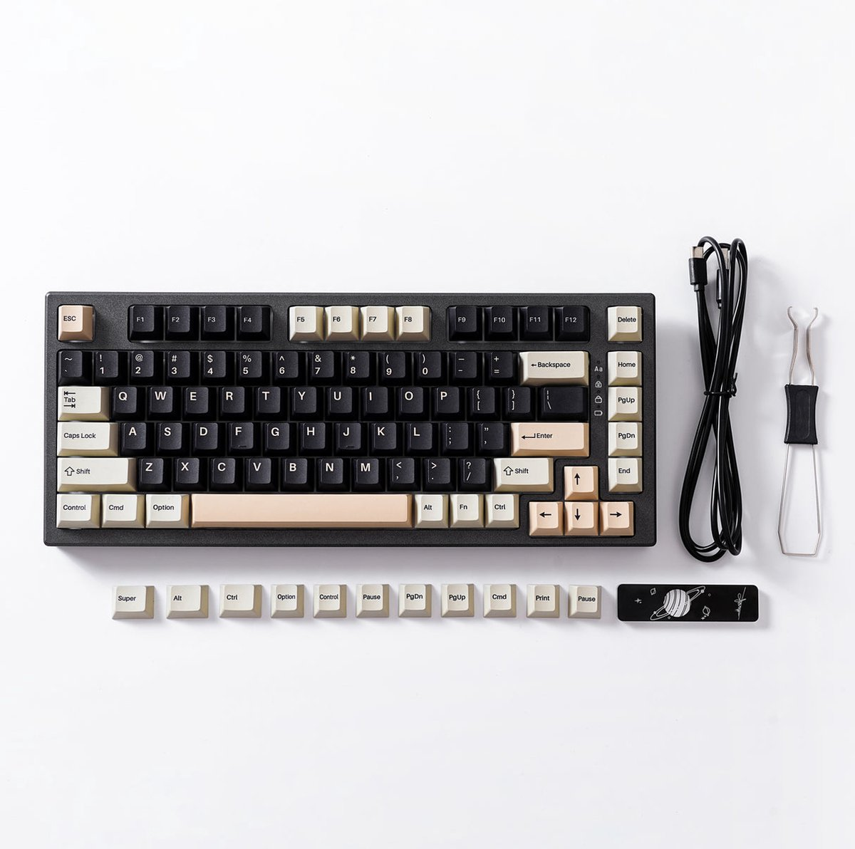 A black and beige mechanical keyboard with extra keycaps, cable, and a keycap puller, on a white surface.