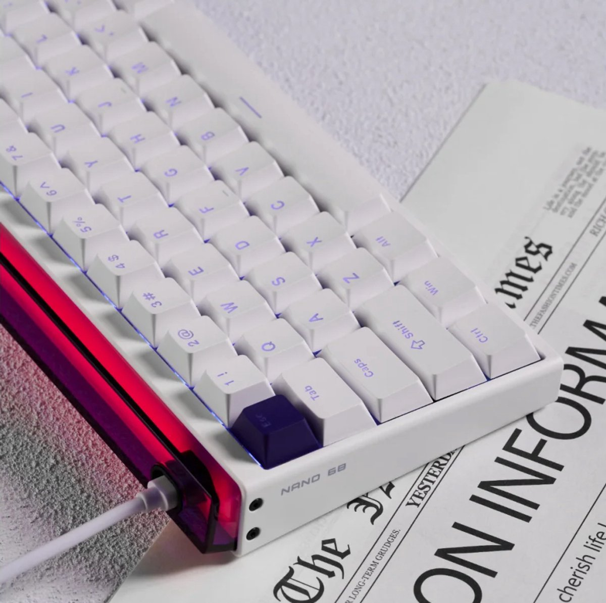 Una tastiera bianca con lettere viola è appoggiata su un giornale. La tastiera ha un accento viola ed è collegata tramite un cavo bianco.