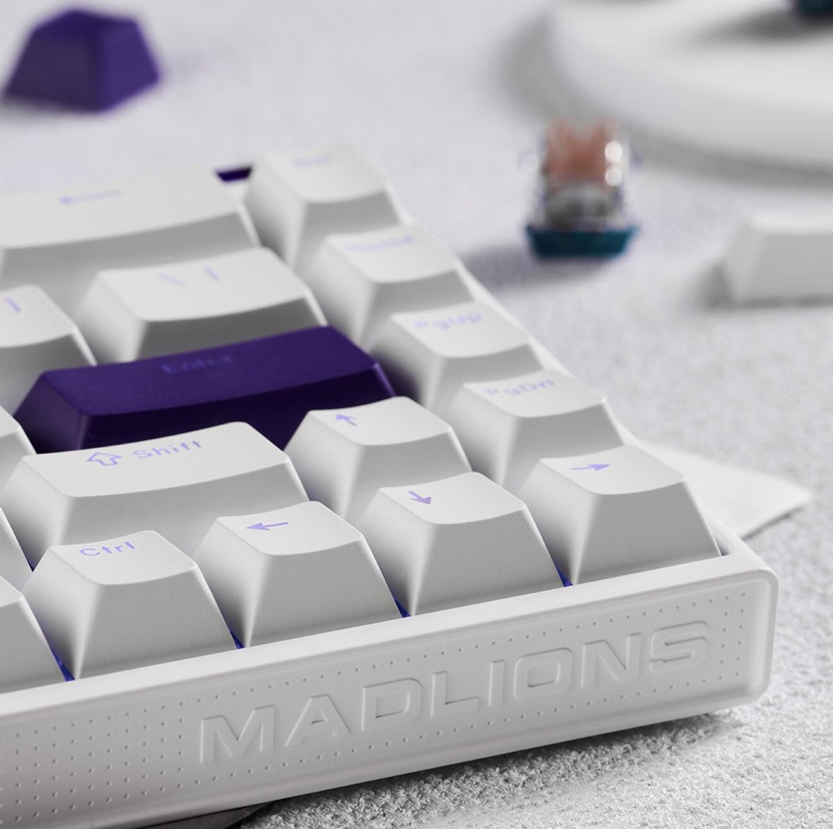 Un primo piano di una tastiera meccanica bianca e viola. I tasti sono bianchi con scritte viola. 'MADLIONS' è visibile.