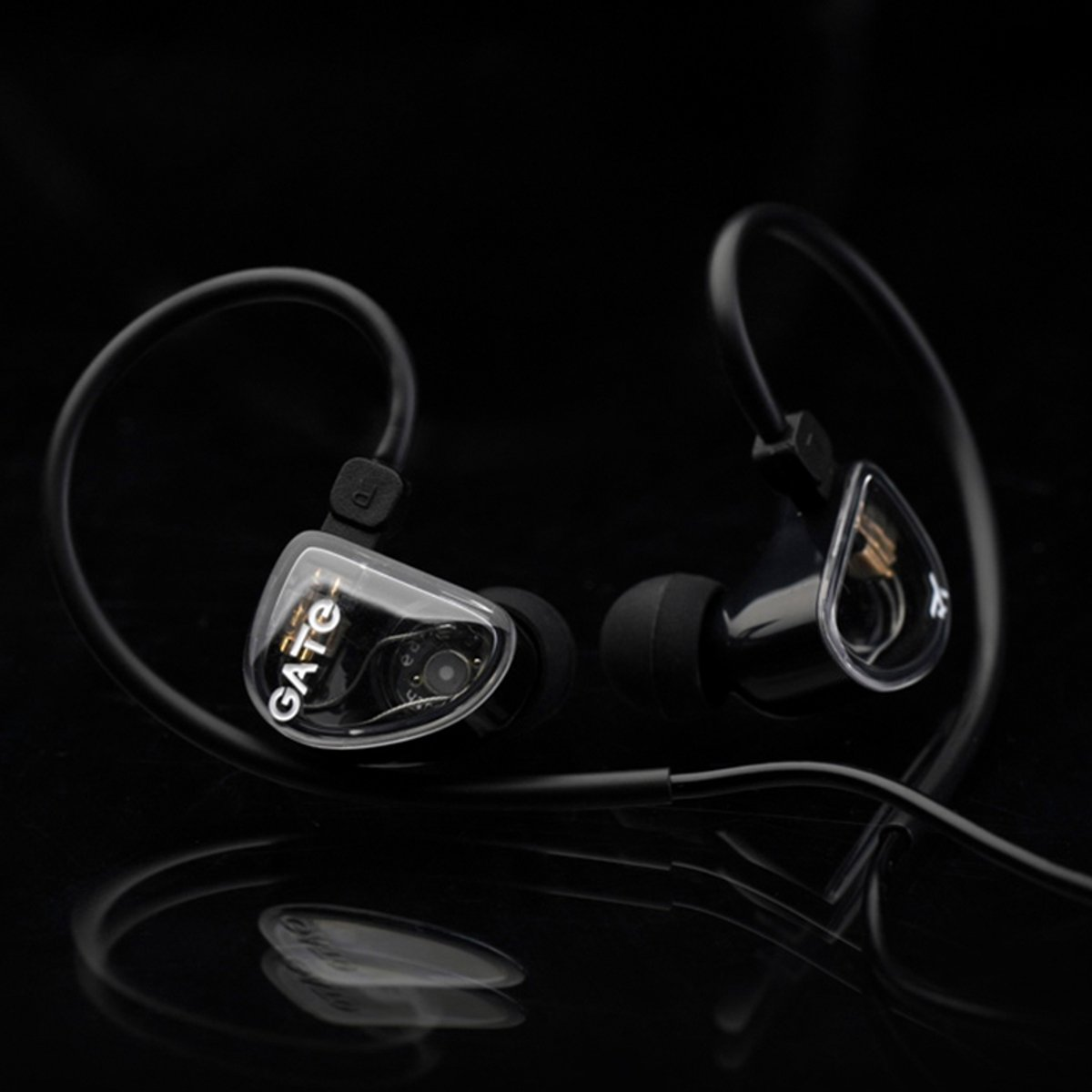 Twee zwarte en doorzichtige in-ear monitors op een reflecterend oppervlak. De linker heeft het woord 'GATE'. Zwarte achtergrond.