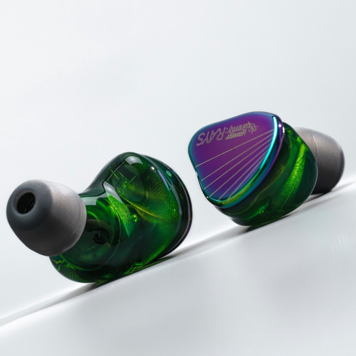 Twee groene en paarse in-ear oortelefoons op een wit oppervlak. Eén oortelefoon is dichterbij met een grijze punt.