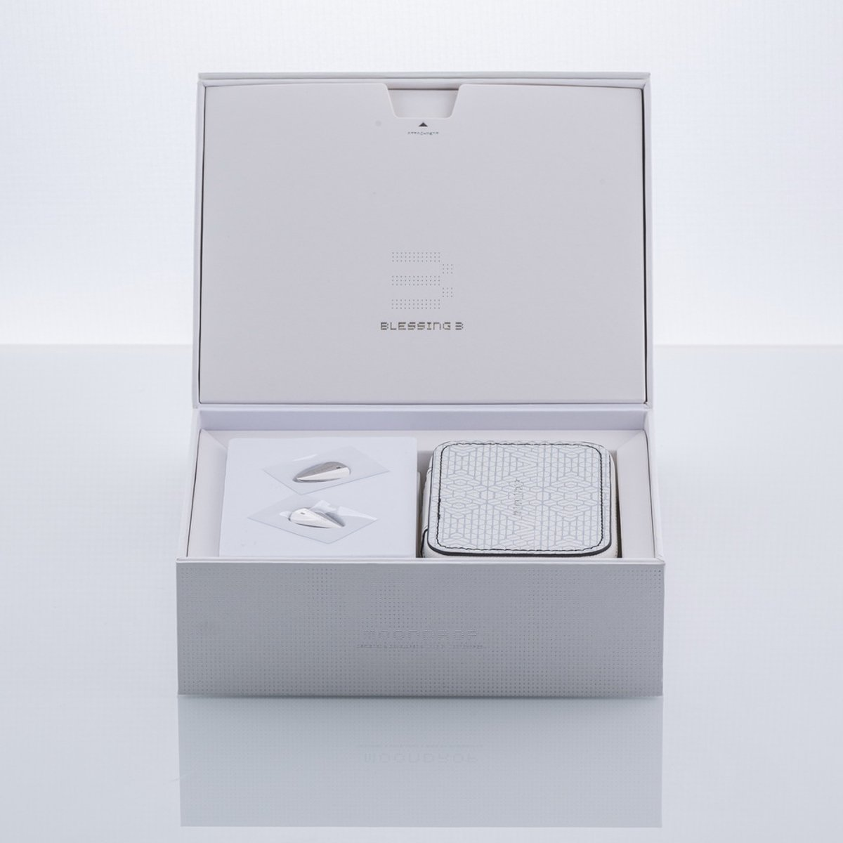 Open witte doos met producten erin. Bevat een vierkant item, twee zilveren objecten en de tekst 'BLESSING 3'.