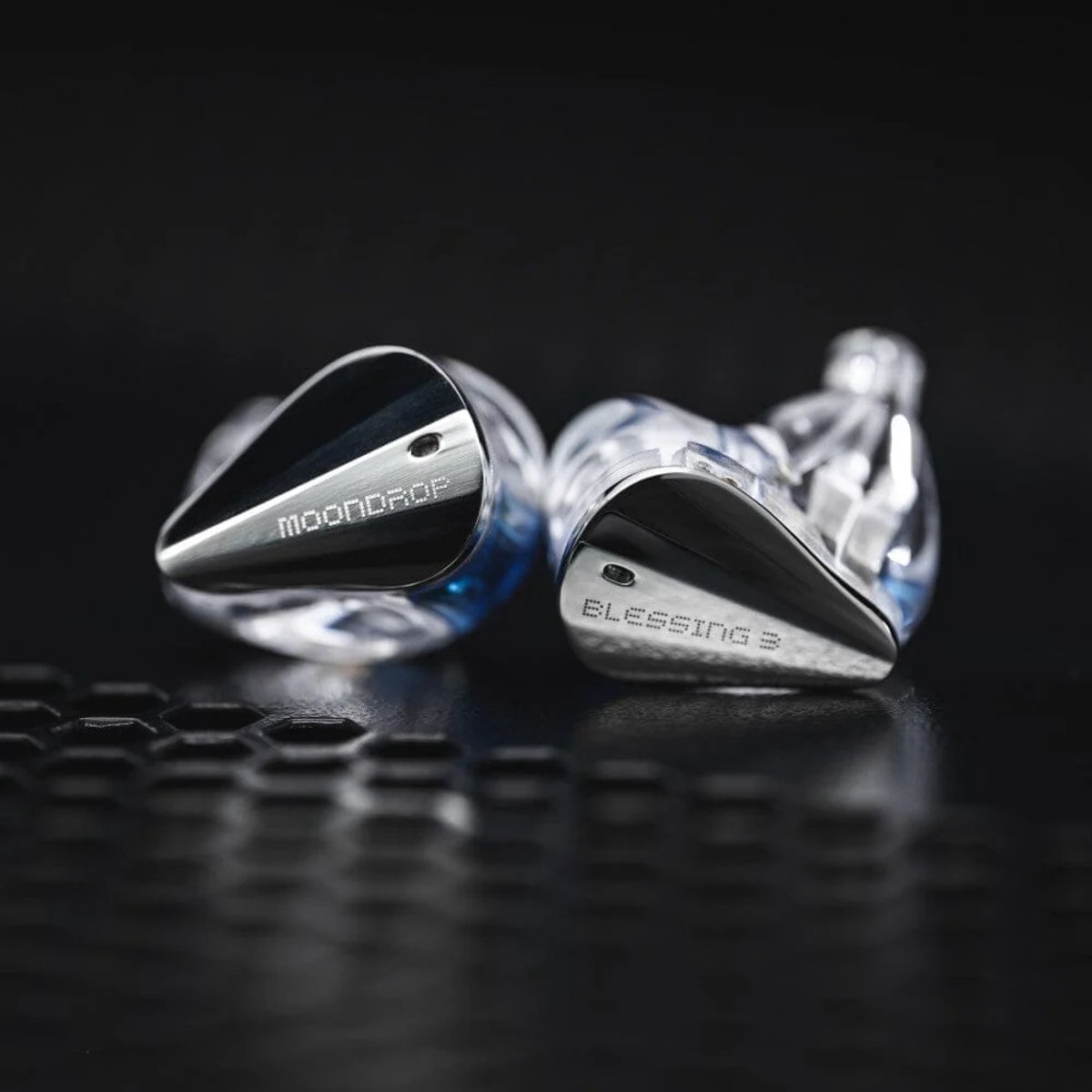 Twee in-ear monitors. Eén zegt MOONDROP, de andere BLESSING 3. Beide zijn zilver en zwart met een transparant gedeelte.