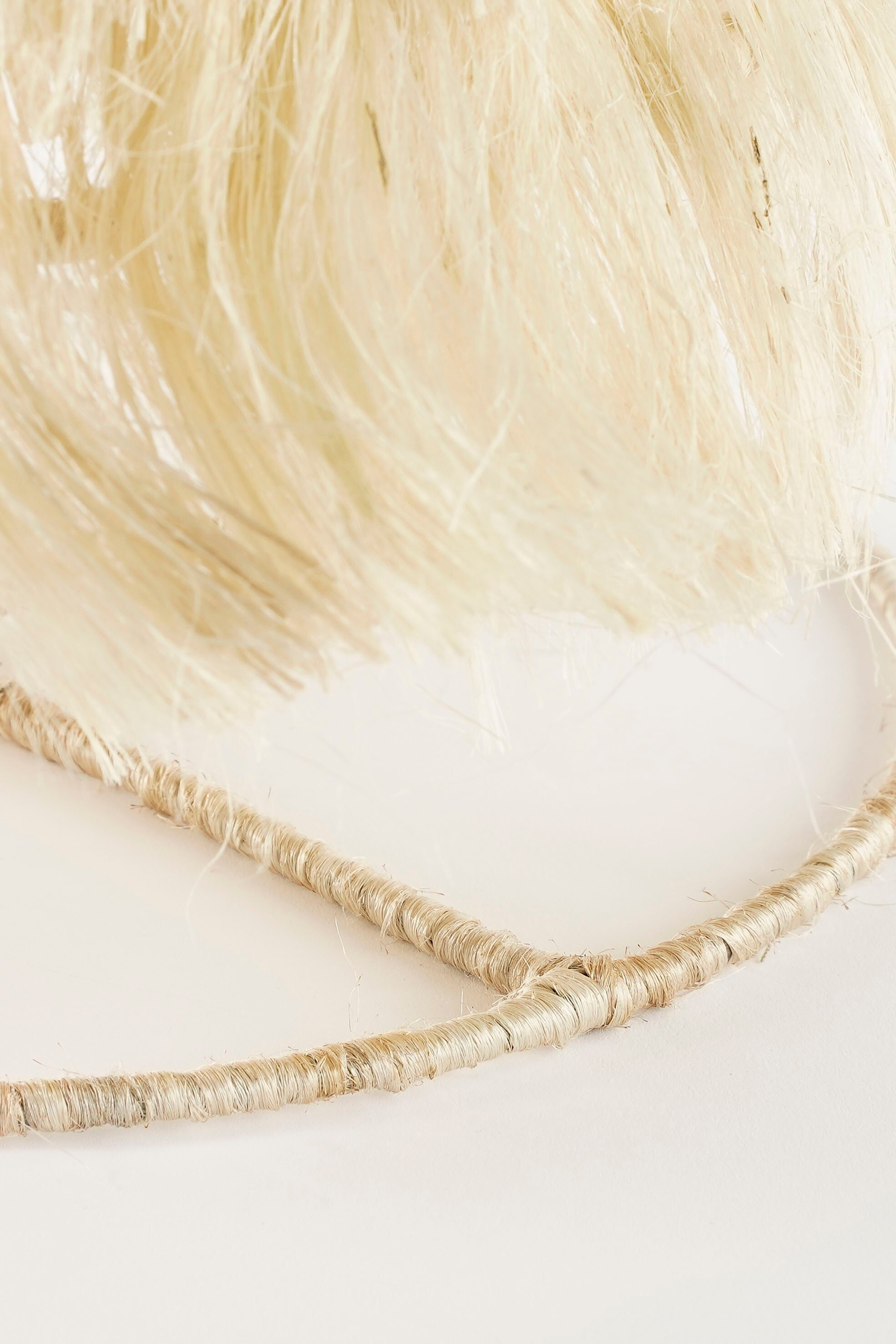 Gros plan d'un objet en fibres naturelles avec des détails texturés, couleur beige clair, sur fond blanc.