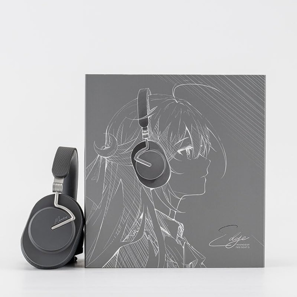 Graue Kopfhörer neben einer grauen Box mit einer Anime-Zeichnung einer Frau mit Kopfhörern. Weißer Hintergrund.