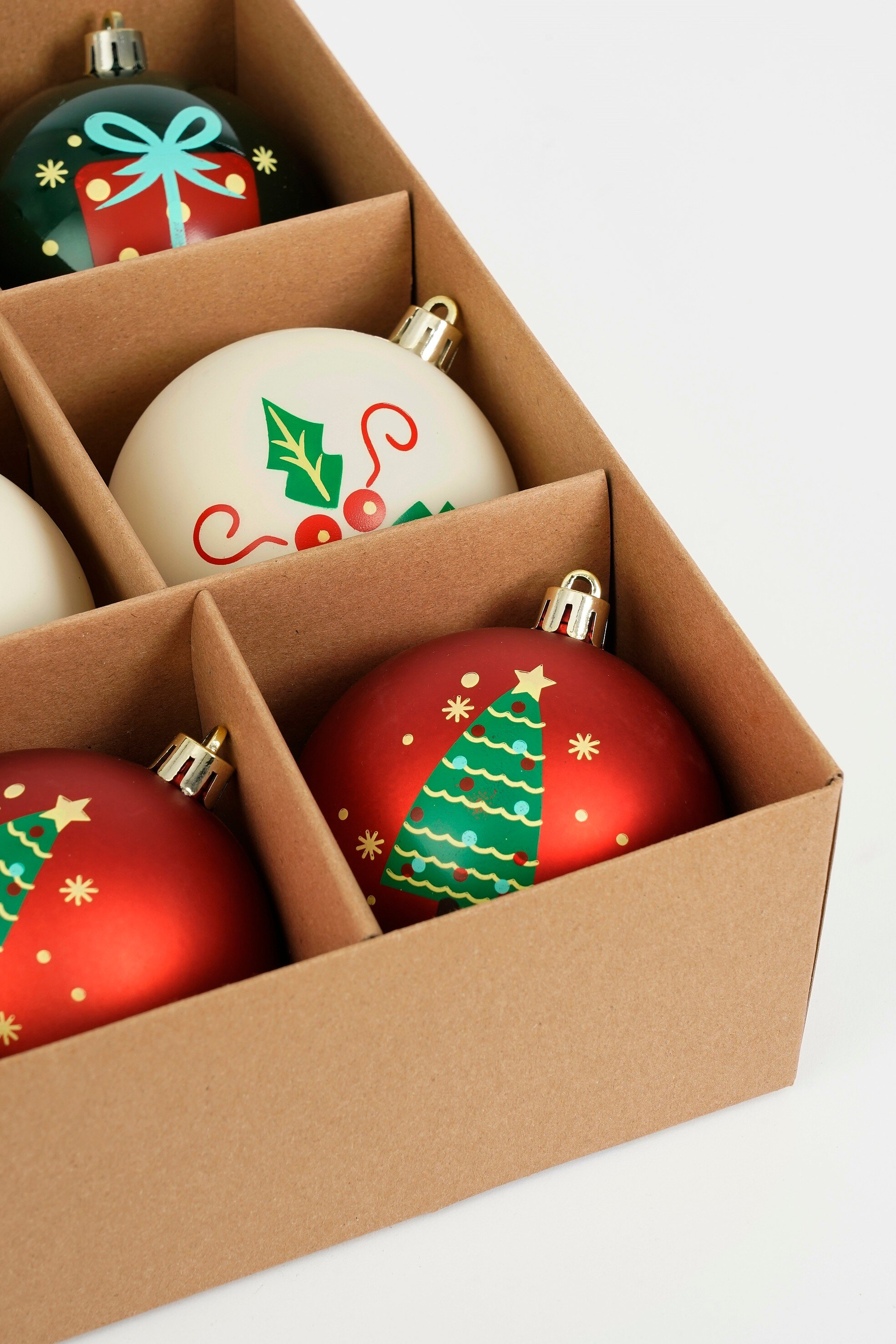 Une boîte contient des ornements de Noël. Il y a des ornements verts, blancs et rouges avec divers motifs festifs.