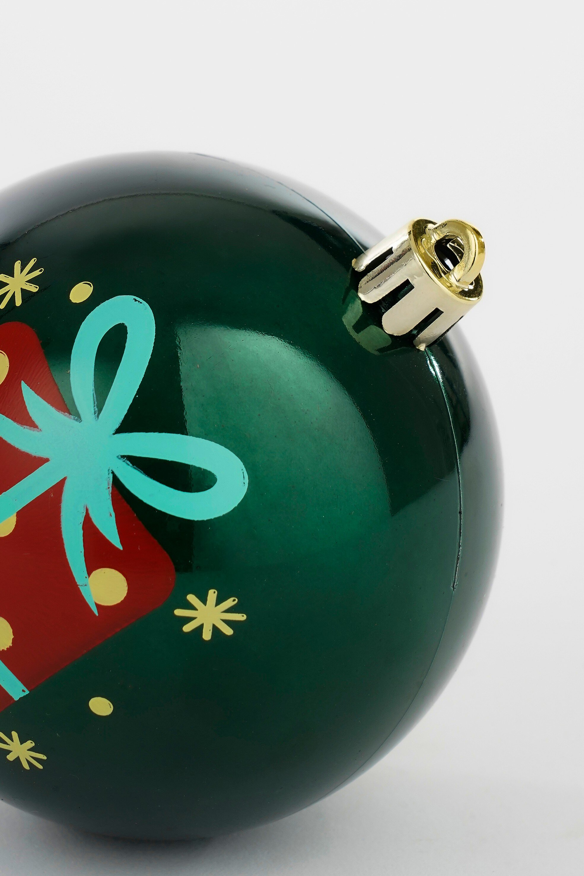 Ornement de Noël vert avec un motif de cadeau rouge et un nœud turquoise. Bouchon doré en haut. Fond blanc.