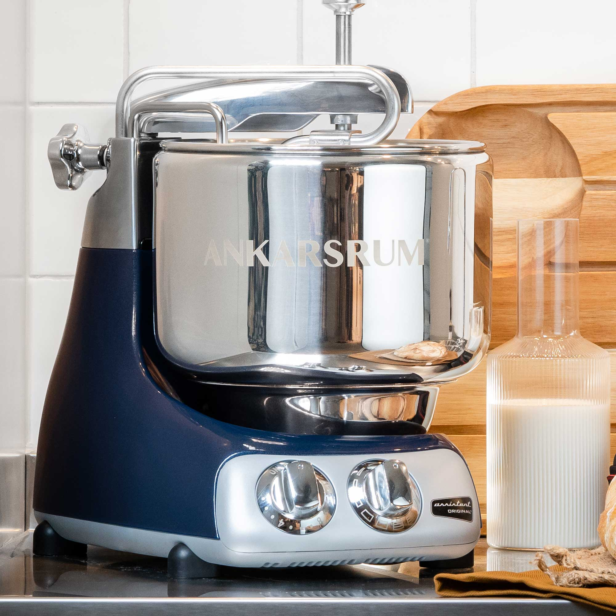 Ein blauer und silberner Küchenmixer steht auf einer Theke. Eine Milchflasche und ein Holzbrett liegen daneben.
