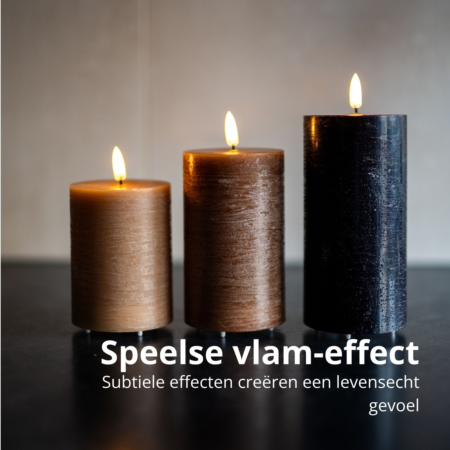 Drie brandende pilaar kaarsen, bruin, brons en zwart, staan op een donkere ondergrond. Vlammen gloeien. Tekst: Speels vlameffect.