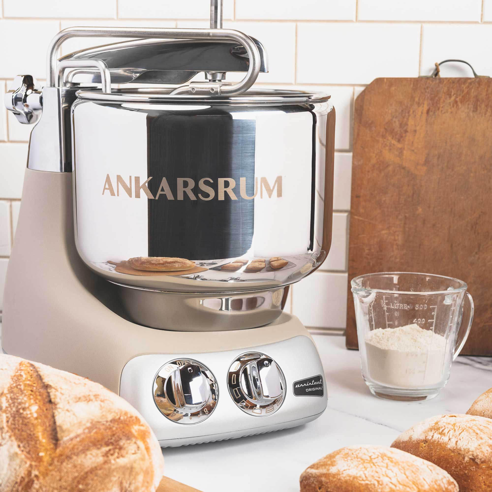 Ein beiger und silberner Küchenmixer mit Brot und Mehl. Ein hölzernes Schneidebrett ist im Hintergrund.