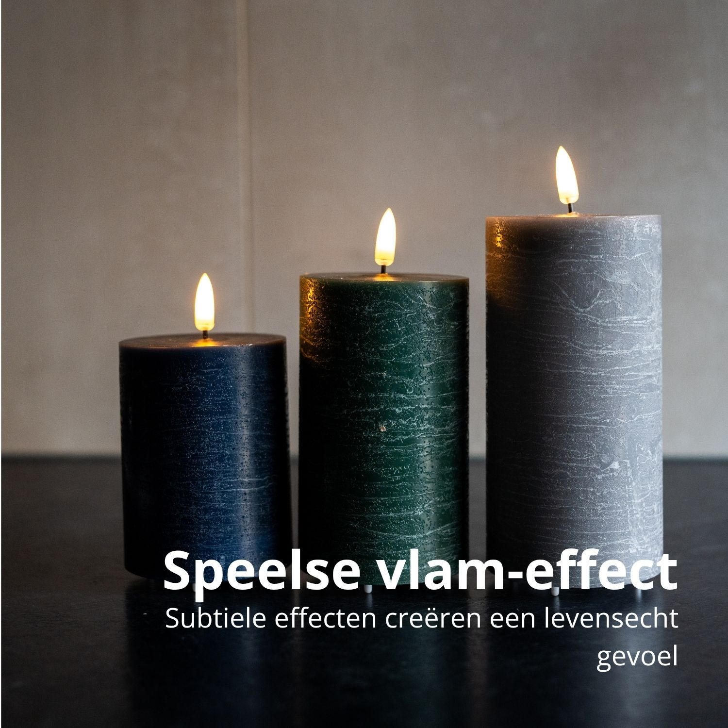 Drei brennende Kerzen, blau, grün und grau, stehen auf dunkler Oberfläche. Die Flammen flackern vor neutralem Hintergrund.