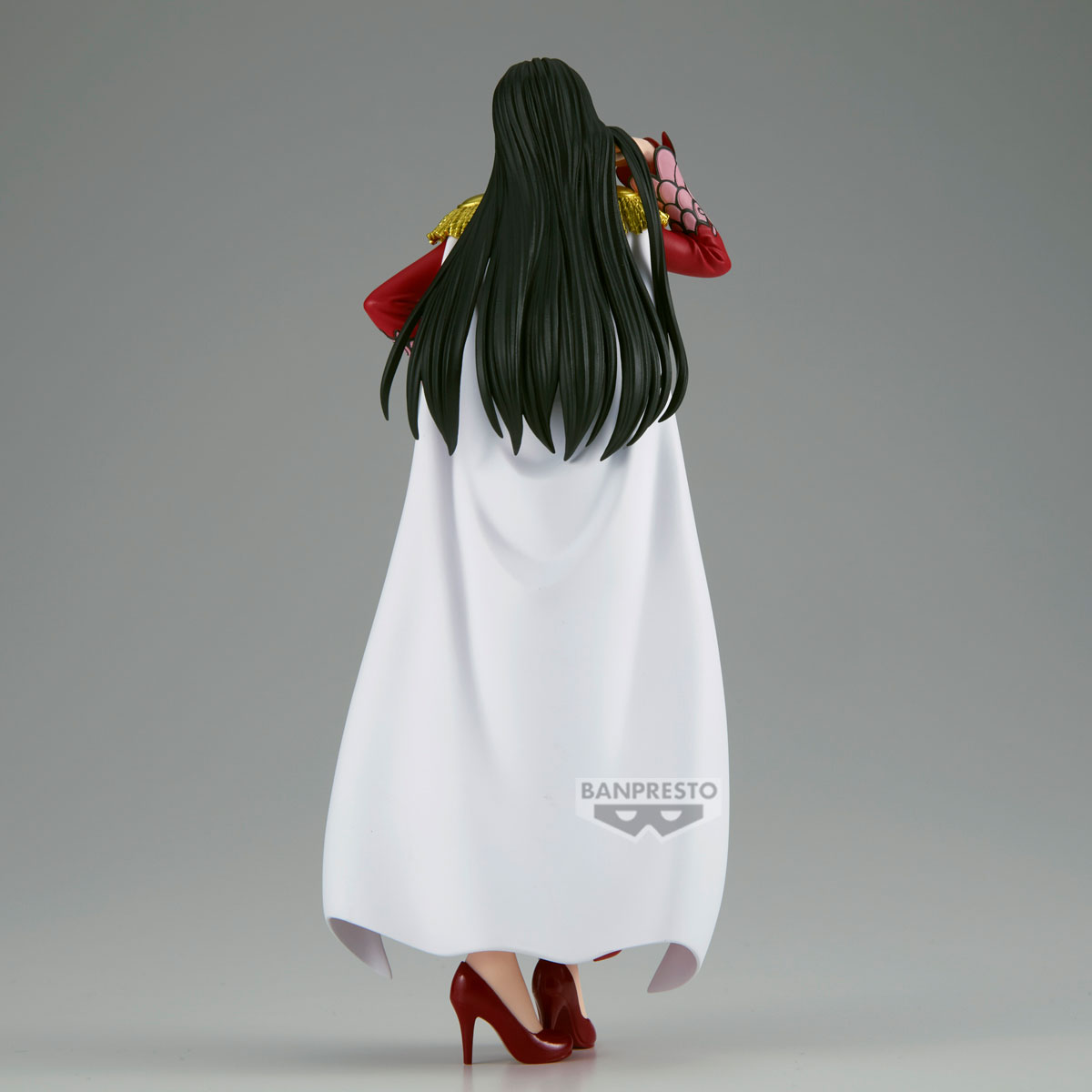 Figura de mujer de espaldas. Lleva capa blanca, tacones rojos y pelo largo negro. Se ven detalles dorados.