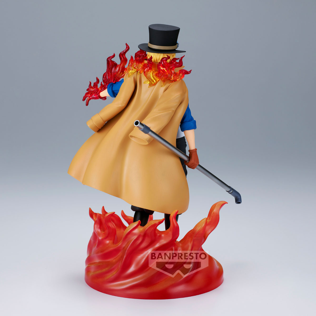 Figura di un uomo con cappotto e cappello a cilindro con fuoco attorno. Tiene una pipa e si trova su una base infuocata.