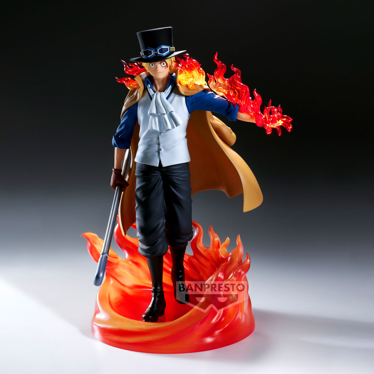 Figura di Sabo con effetti di fuoco. Indossa un cappello a cilindro, un mantello e tiene un bastone. Le fiamme circondano la mano e la base.