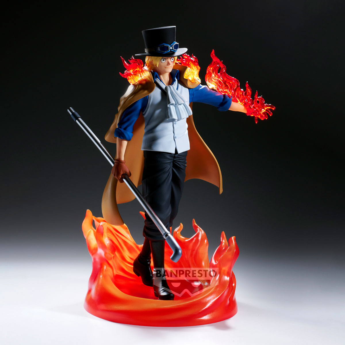 Figura di un uomo con capelli biondi, cilindro e fiamme. Tiene un bastone e si trova su una base di fuoco. È vestito di blu, bianco e nero.