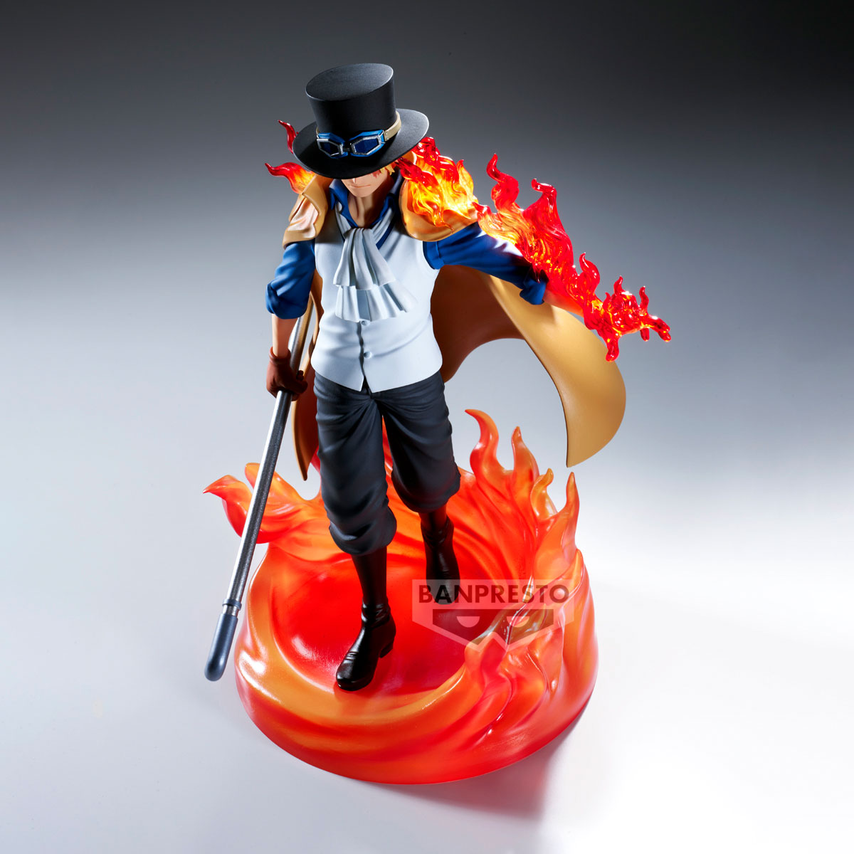 Una figura di un uomo con cappello e mantello, circondato dalle fiamme. Tiene un bastone. La figura è su una base infuocata.