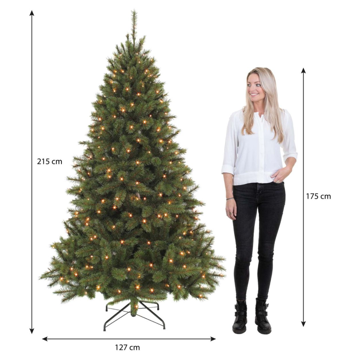 Een vrouw staat naast een verlichte kerstboom. De boom is 215 cm hoog en de vrouw is 175 cm. De boom is 127 cm breed.