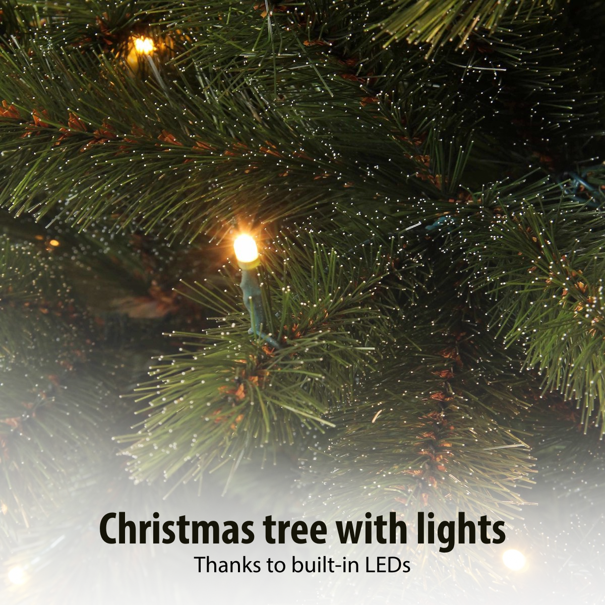 Close-up van een groene kerstboom met kleine witte accenten en warme gele lichten.
