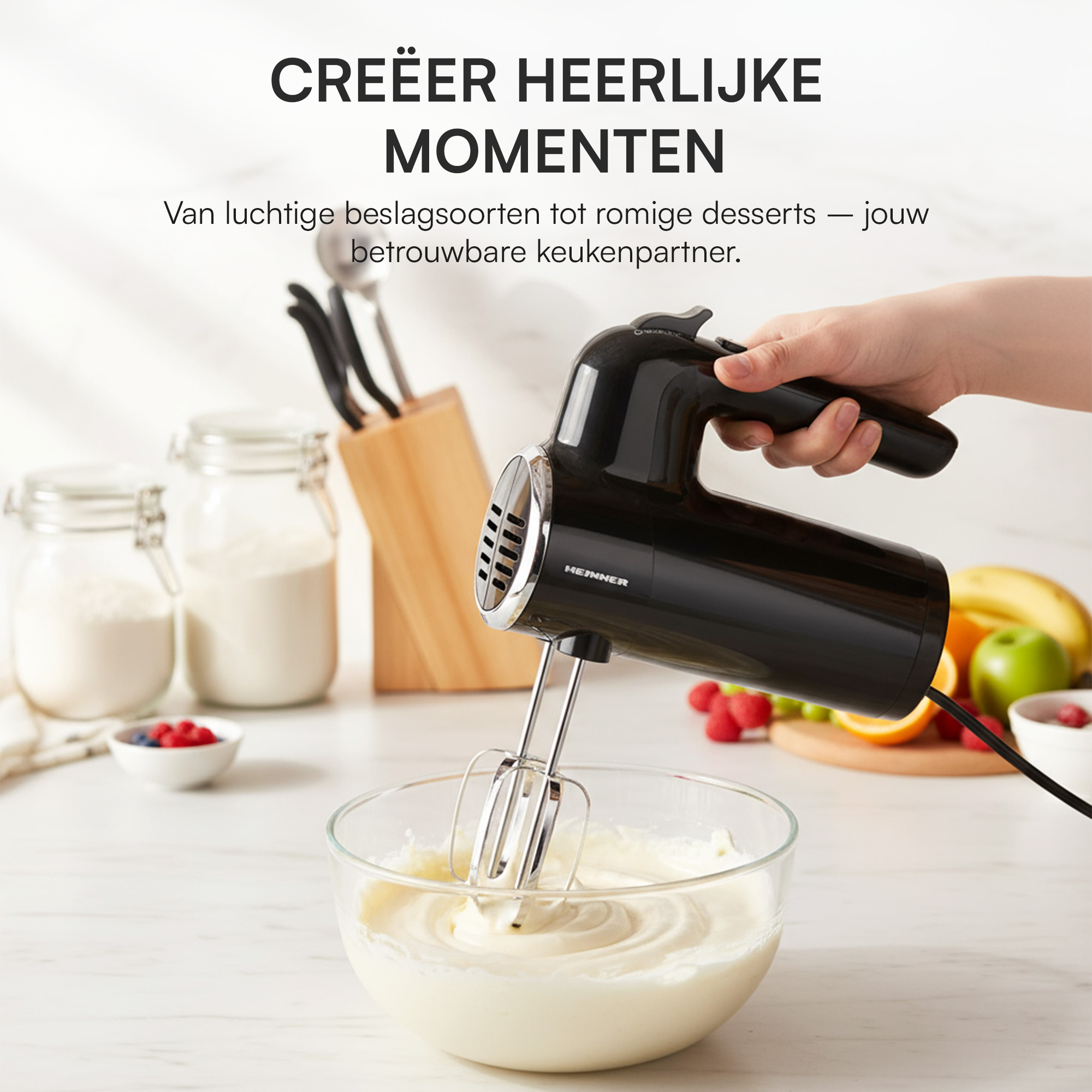 Eine Hand, die einen schwarzen Handmixer über einer Schüssel mit Sahne hält. Früchte und Gläser sind im Hintergrund.