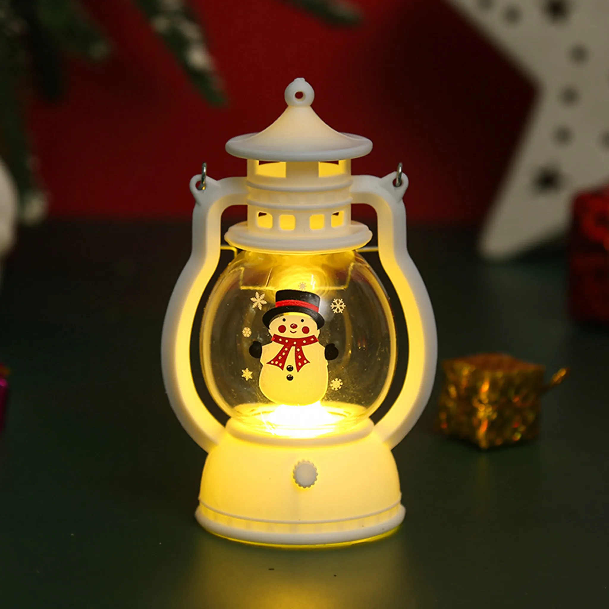 Eine weiße Laterne mit einem Schneemann darin. Es ist beleuchtet. Ein roter Hintergrund und eine goldene Geschenkbox sind dahinter.