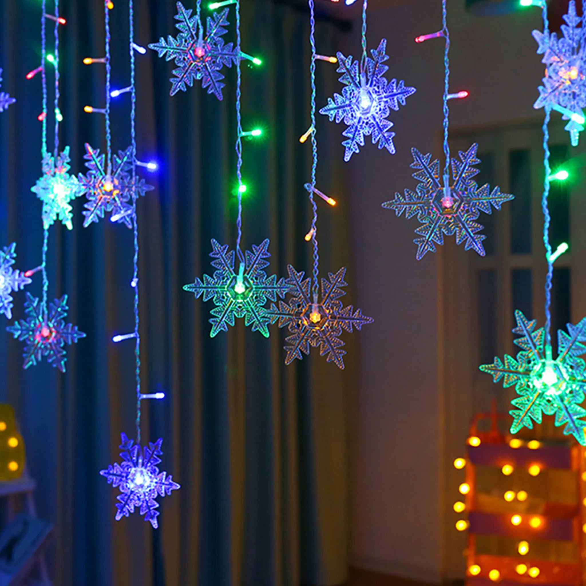 Schneeflockenlichter mit verschiedenen Farben hängen vor einem blauen Vorhang und einem gelben Licht.