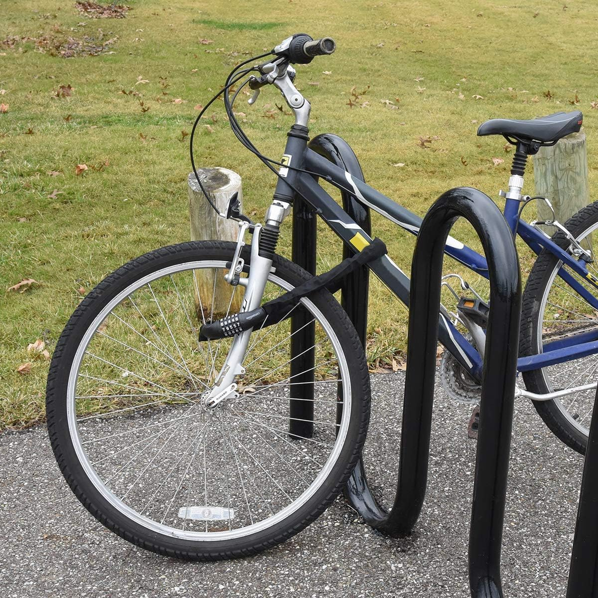 Ein Fahrrad, das mit einem Schloss an einem Fahrradständer gesichert ist. Das Vorderrad ist dem Betrachter am nächsten. Gras und ein Holzpfosten befinden sich im Hintergrund.