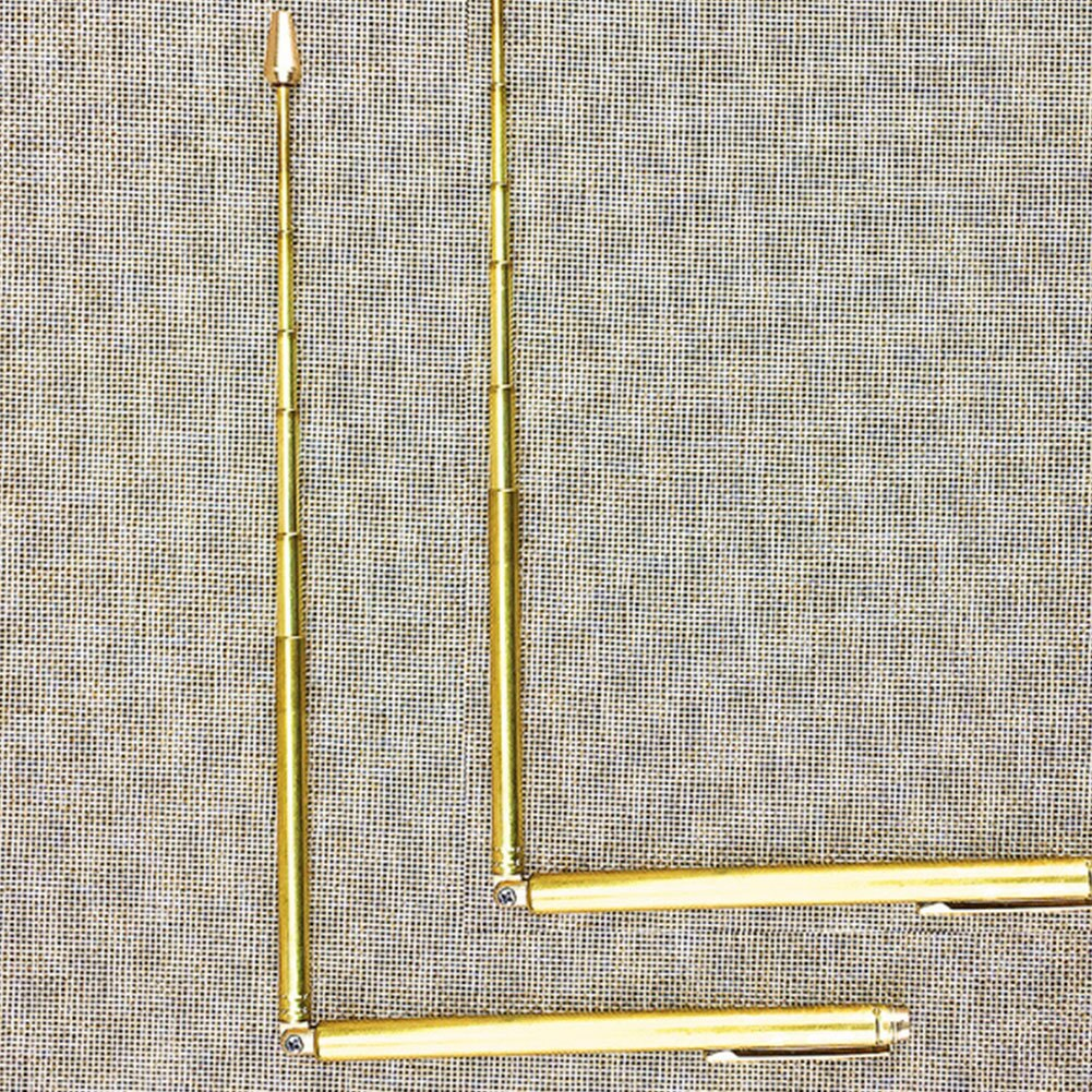 Drei goldene, einziehbare Zeigestäbe auf strukturiertem beigefarbenem Hintergrund. Zwei sind vertikal, einer horizontal, L-Form.