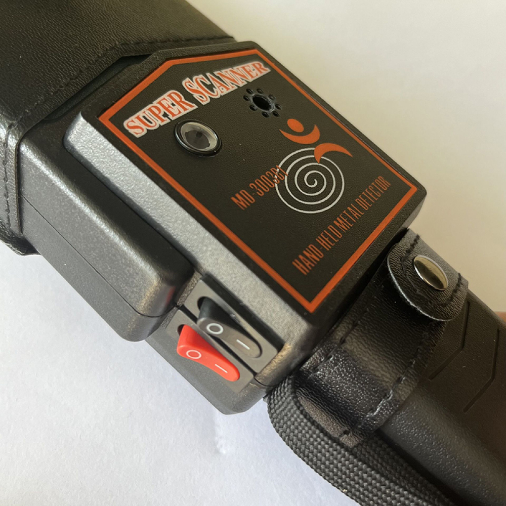 Nahaufnahme eines schwarzen Metalldetektors mit der Aufschrift 'Super Scanner'. Er hat einen roten Schalter und eine Ledertasche.