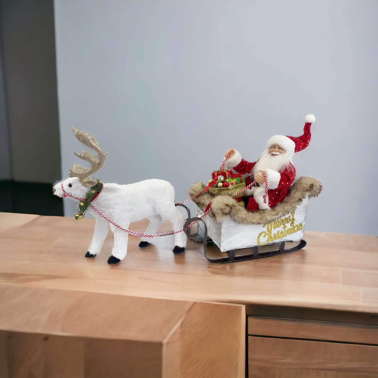 Eine Weihnachtsdekoration zeigt den Weihnachtsmann in einem Schlitten, der von einem Rentier auf einer Holzoberfläche gezogen wird.