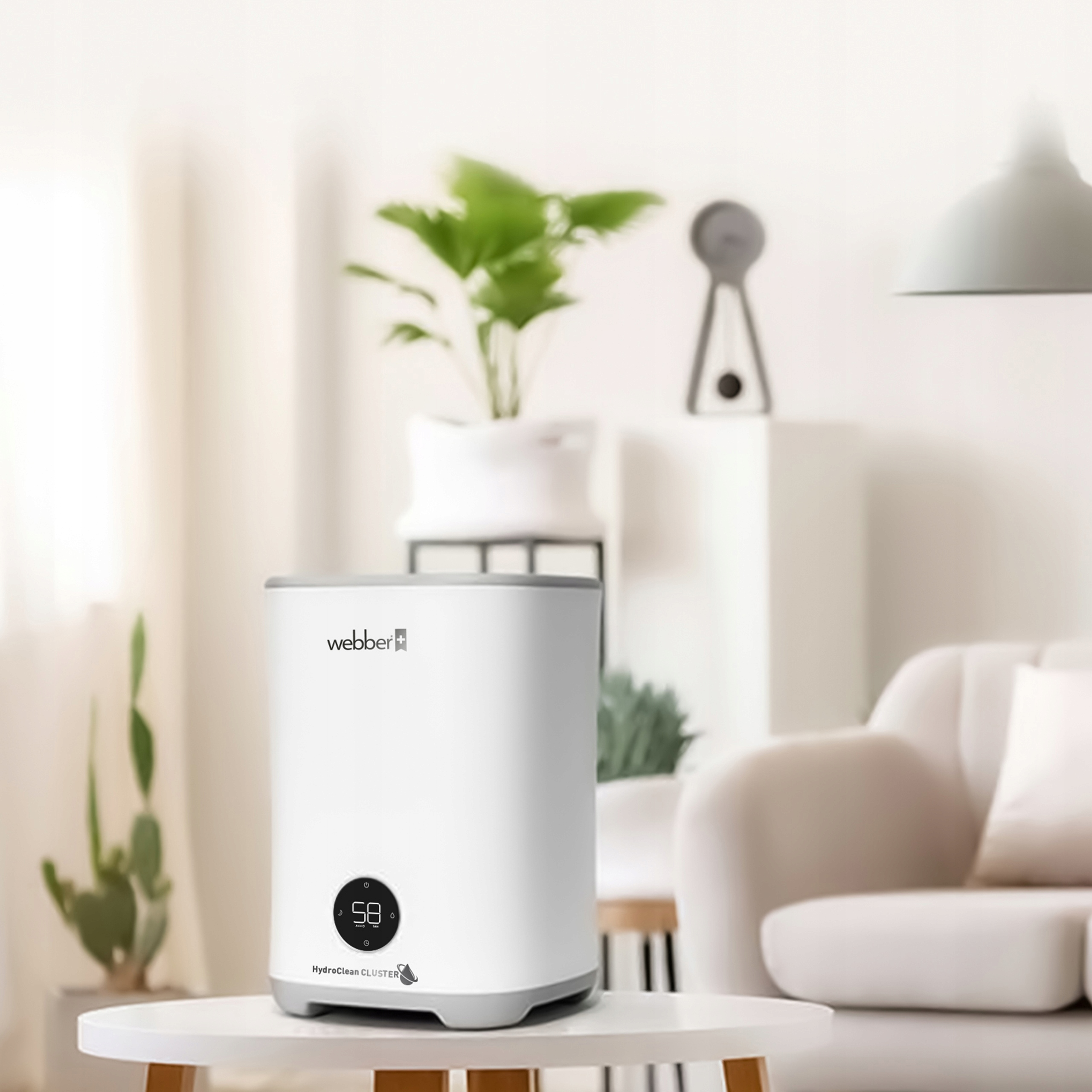 Biały nawilżacz na białym stole. Zielona roślina i sofa w tle. Nawilżacz posiada cyfrowy wyświetlacz.