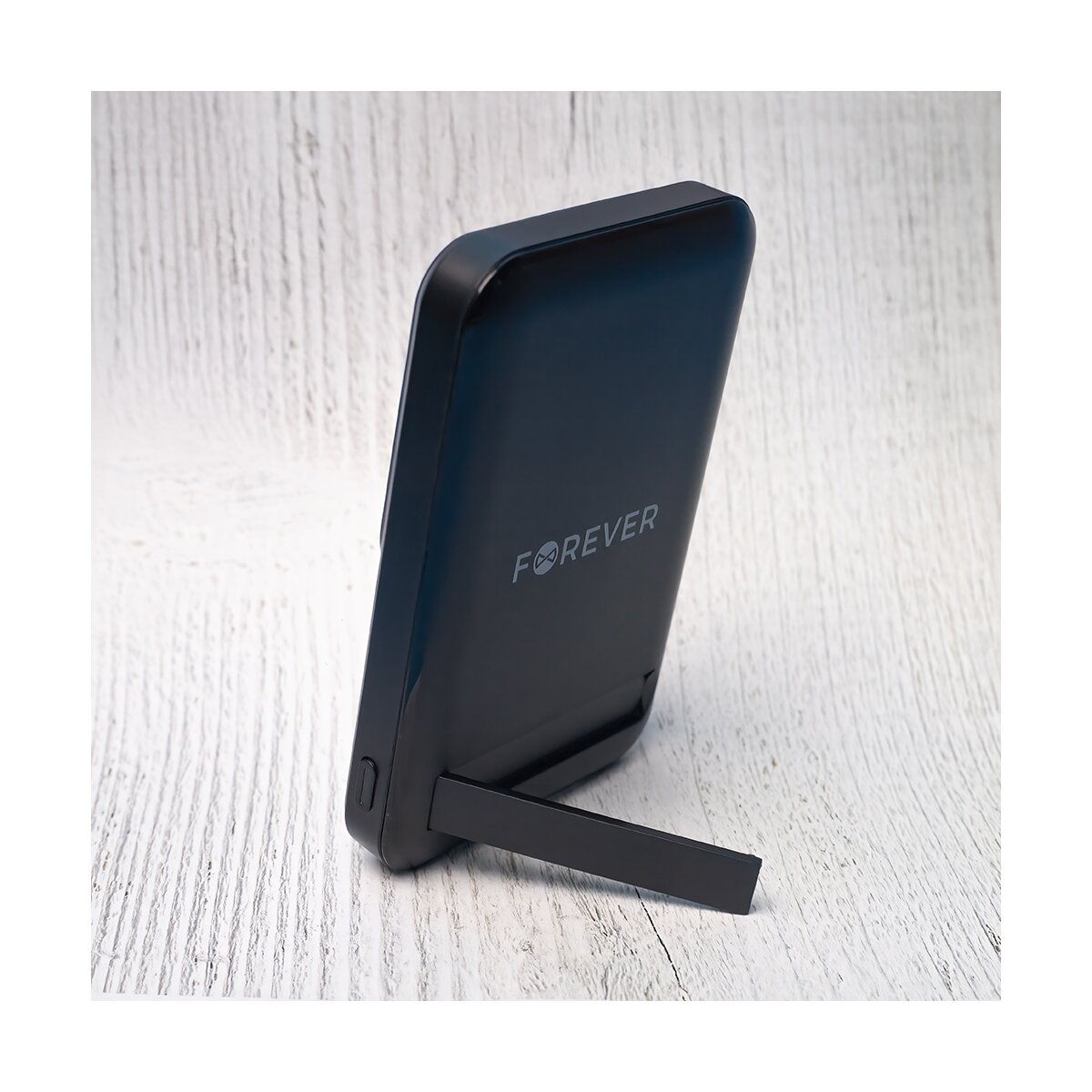 Un dispositivo nero con logo 'FOREVER', sorretto da un supporto, su una superficie di legno bianco.