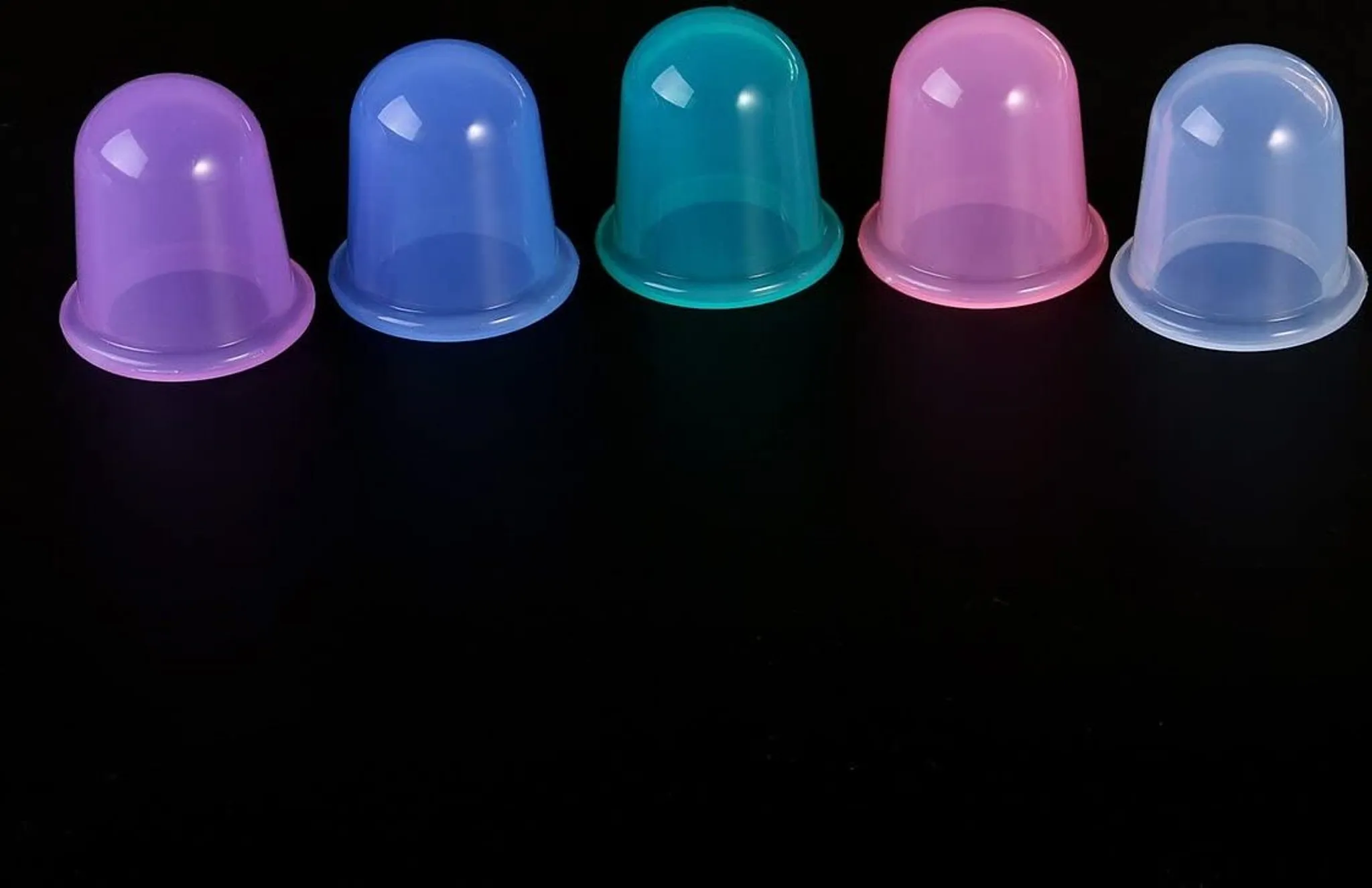 Fünf farbige Schröpftherapiebecher vor schwarzem Hintergrund. Jeder Becher hat eine andere Farbe: Lila, Blau, Grün, Rosa und Hellblau.