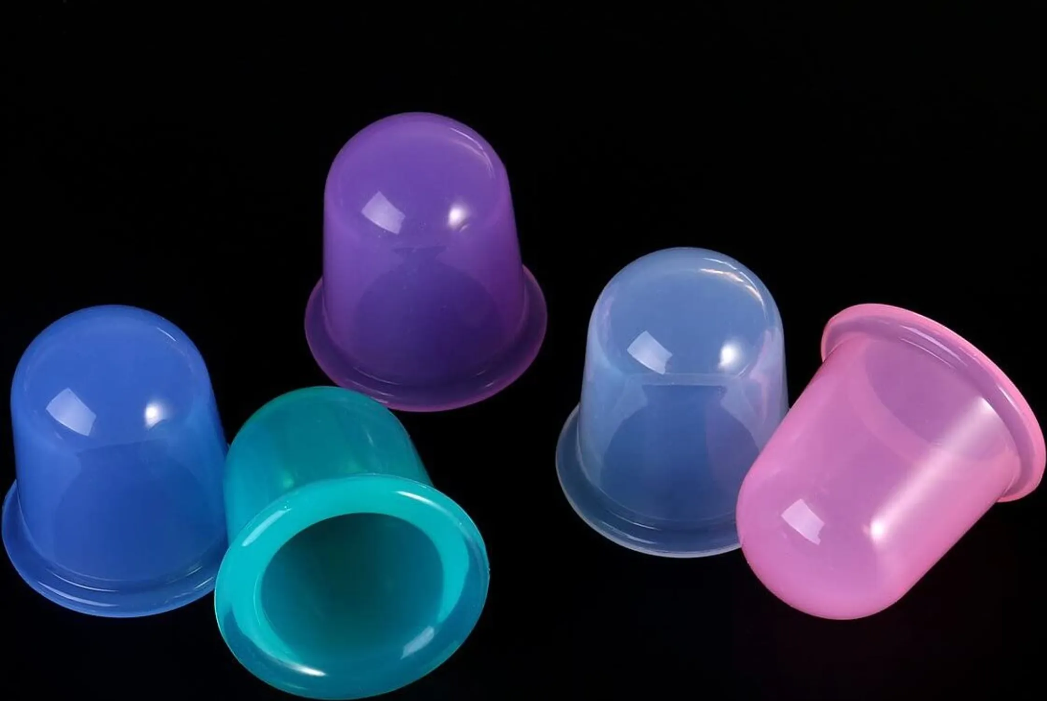 Fünf farbige Schröpftherapie-Becher vor schwarzem Hintergrund. Die Becher sind in verschiedenen Blau-, Grün-, Lila- und Rosatönen gehalten.