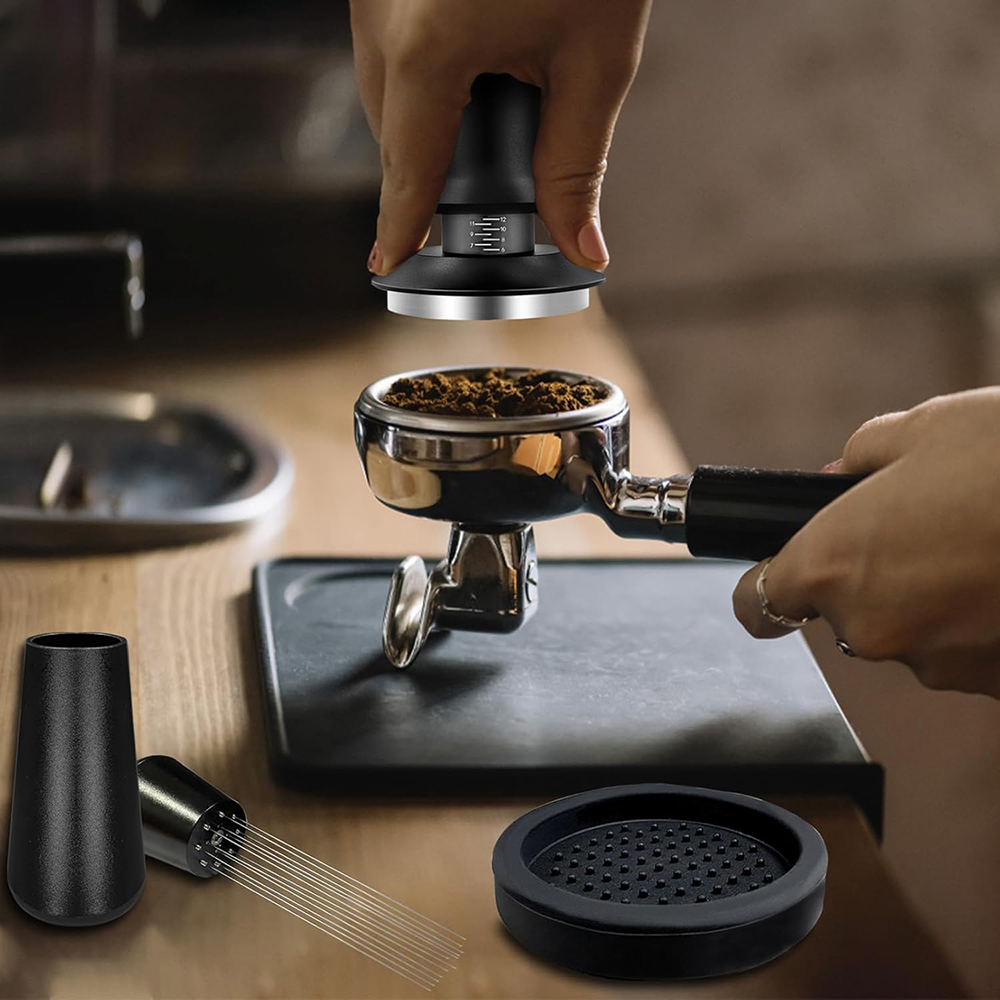 Eine Person verwendet einen Kaffeestampfer auf einem mit Kaffeepulver gefüllten Siebträger. Weitere Werkzeuge zur Kaffeezubereitung sind im Vordergrund.