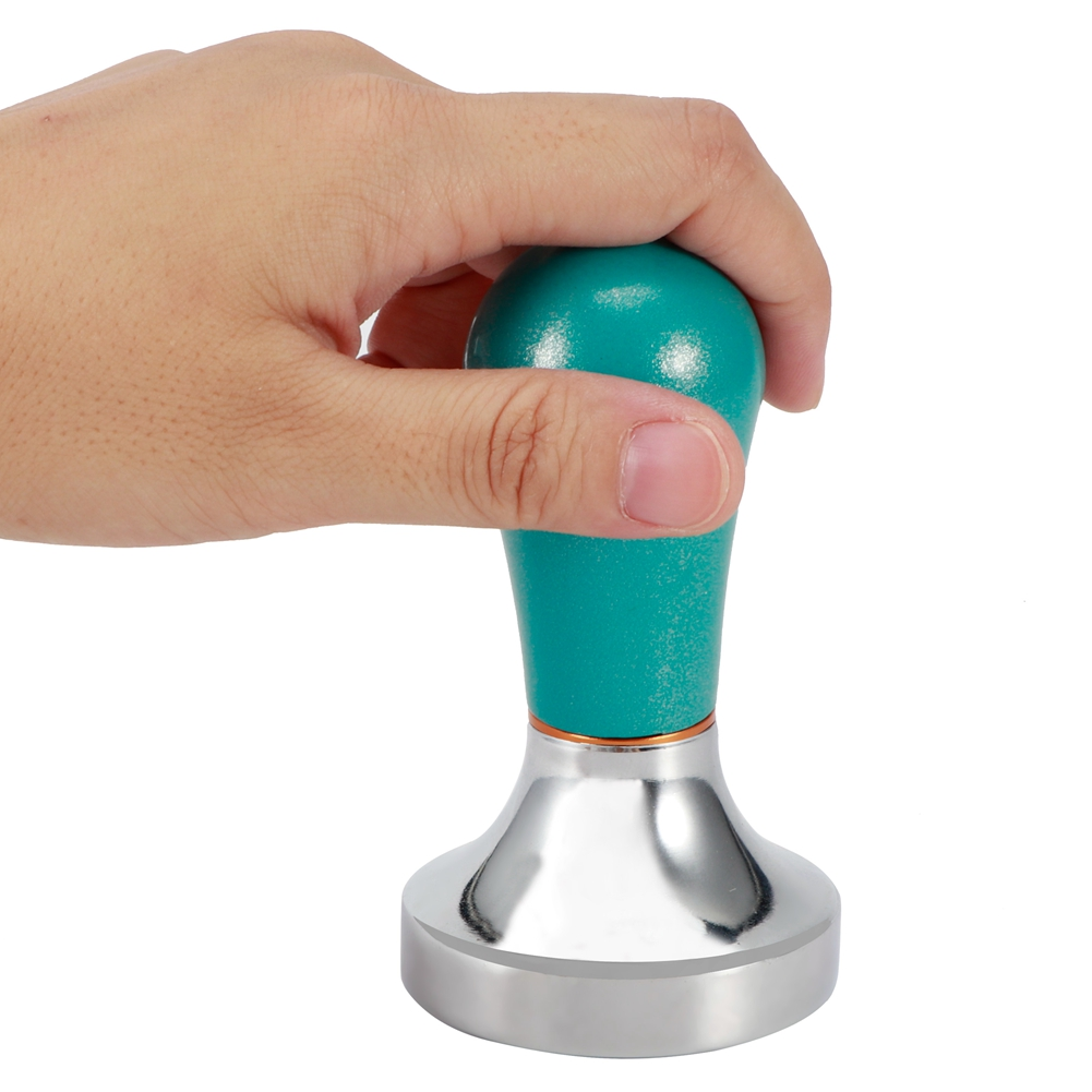 Eine Hand hält einen türkisfarbenen Kaffeestampfer. Der Tamper hat einen silbernen Boden und einen türkisfarbenen Griff. Der Hintergrund ist weiß.