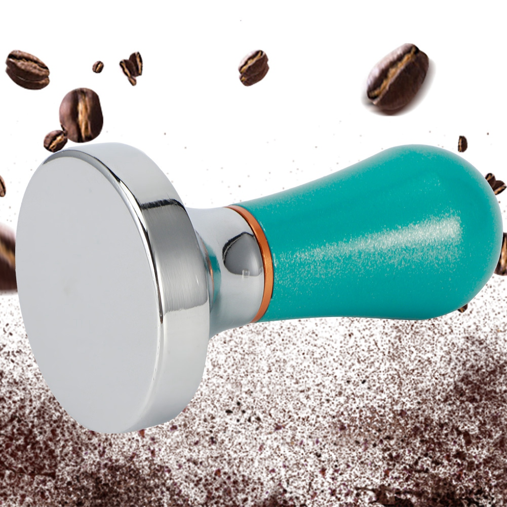 Ein Kaffeestempel mit türkisfarbenem Griff und glänzender Metallbasis. Kaffeebohnen sind verstreut, Kaffeepulver im Hintergrund.