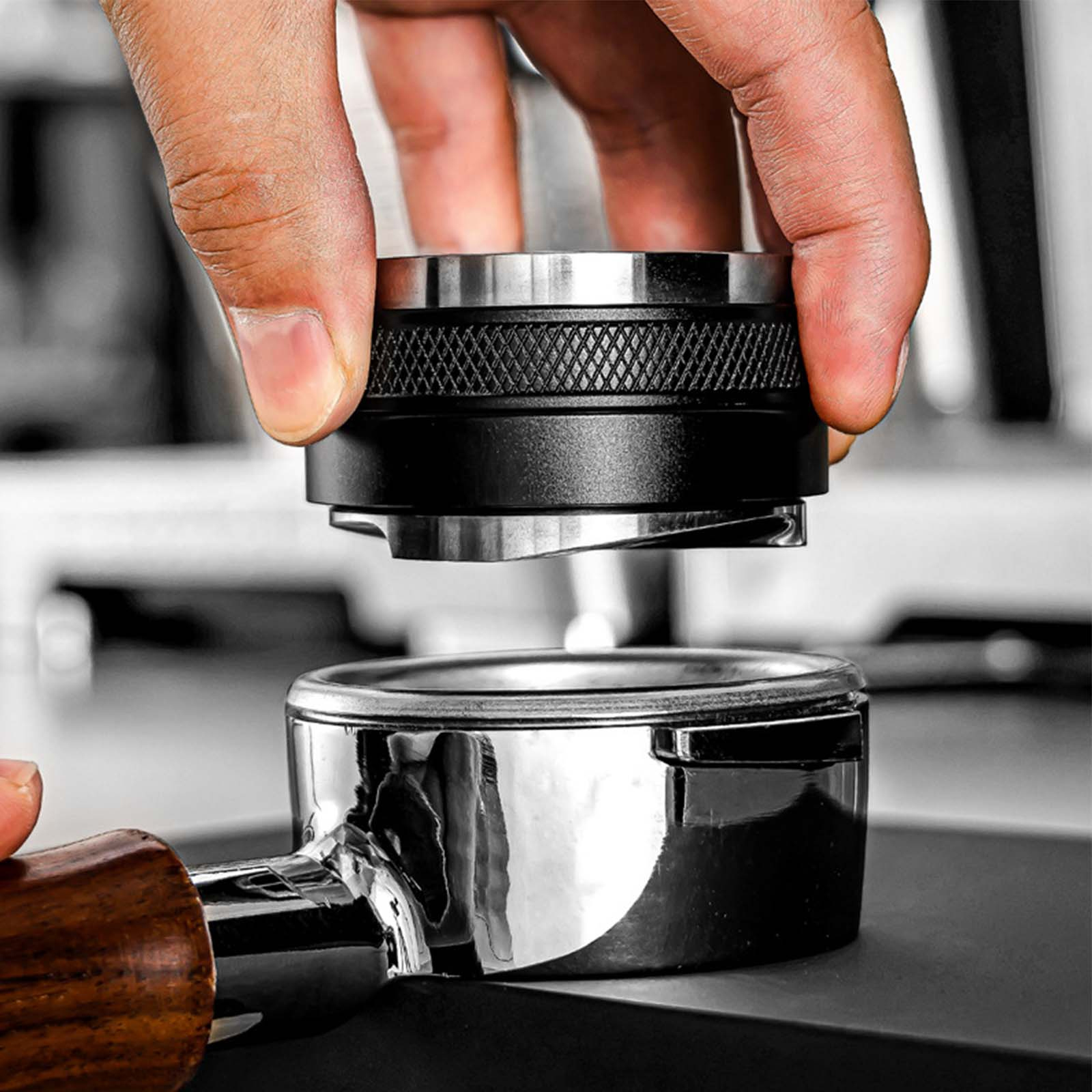Eine Hand hält einen Kaffeestampfer über einem Siebträger. Der Tamper ist schwarz und silber.