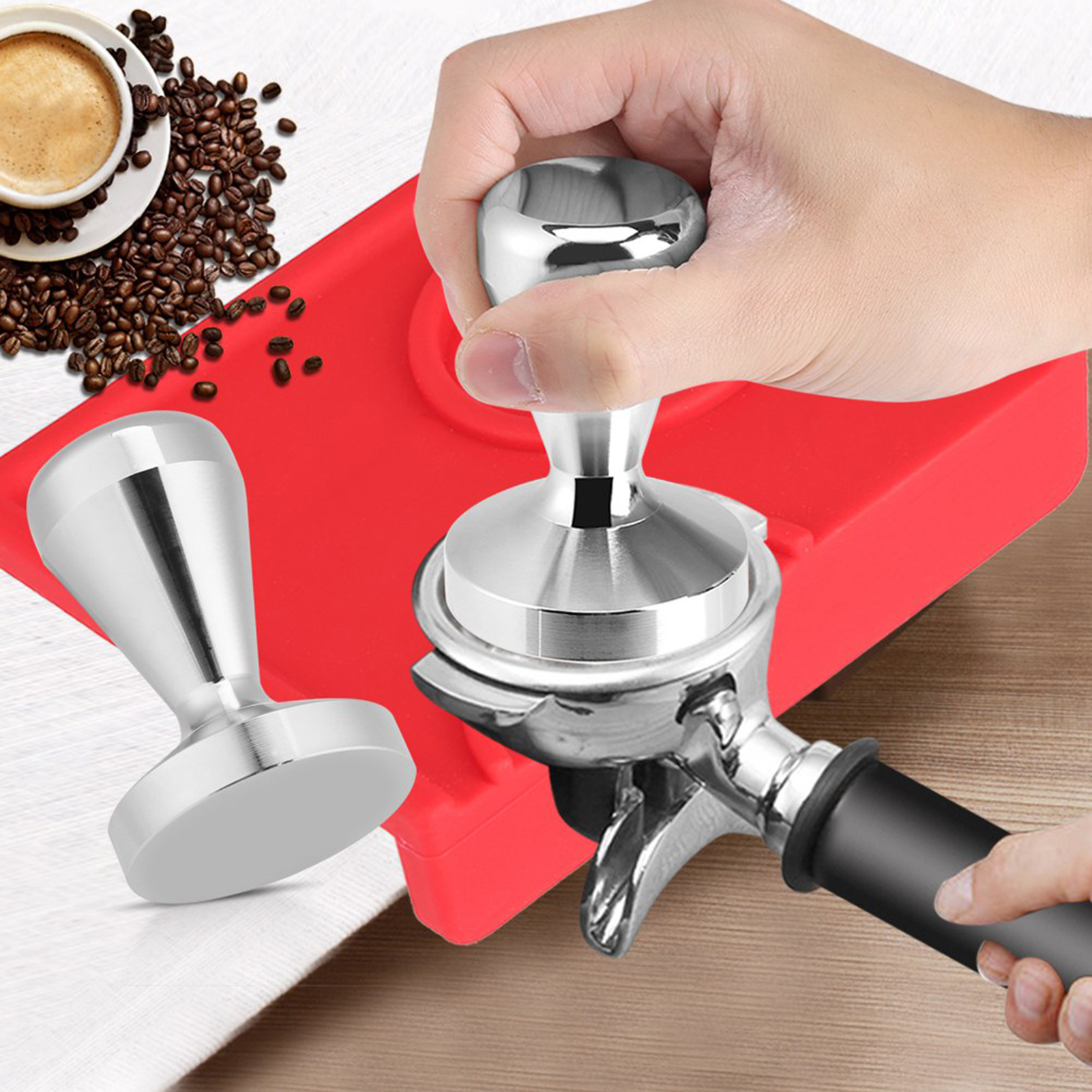 Eine Hand drückt einen Tamper auf einen Espresso-Maschinen-Siebträger, daneben Kaffeebohnen und eine Kaffeetasse.